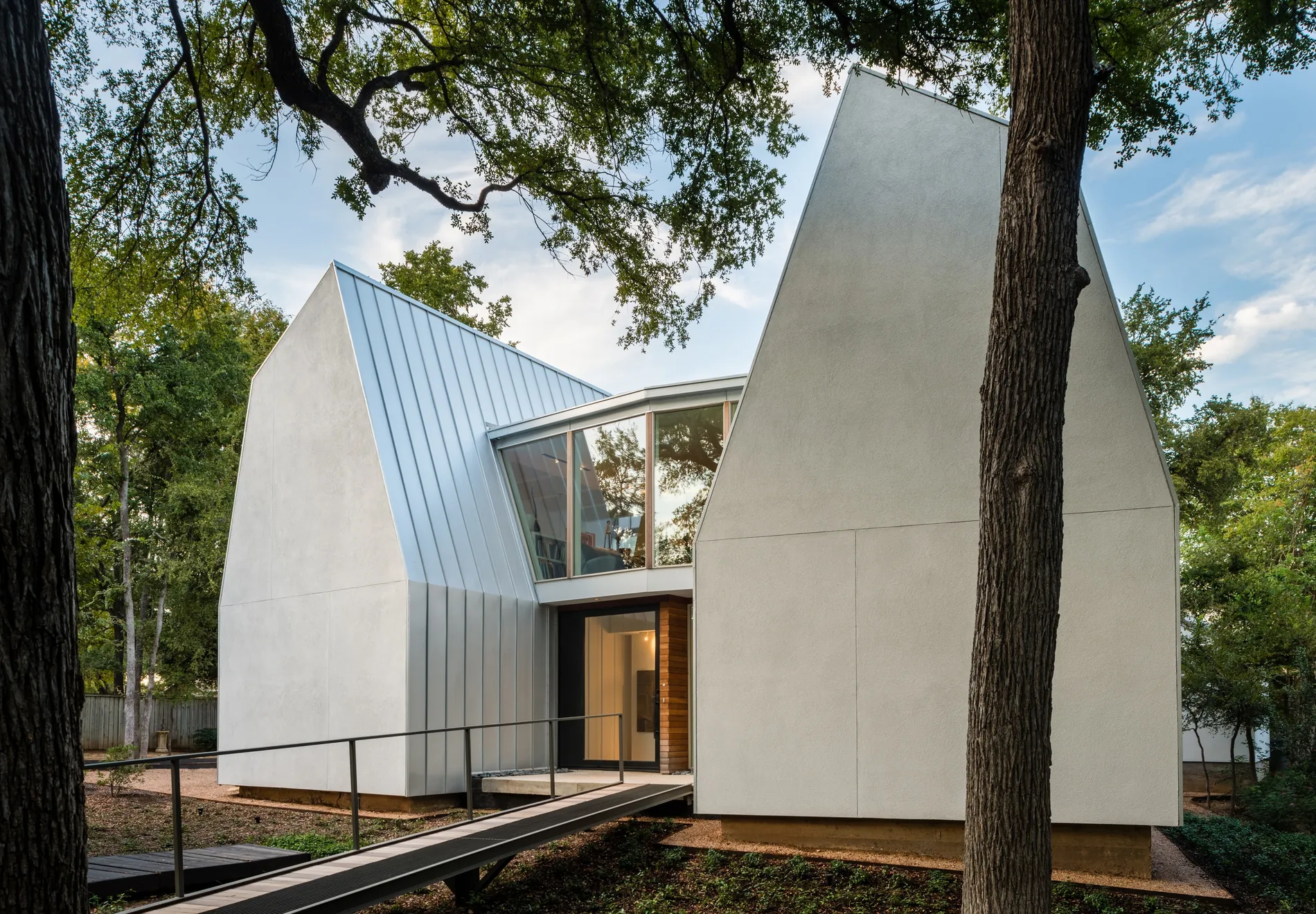 Award-winning SIP residence with dramatic white gabled forms set among mature trees